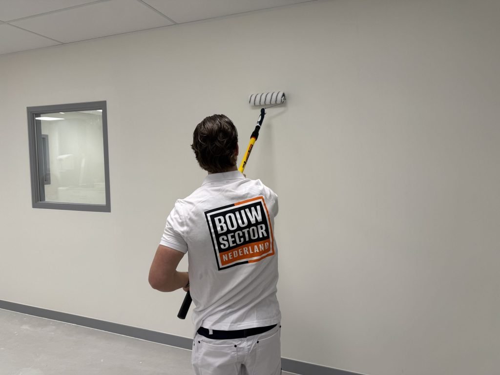 Schilder van Bouwsector Nederland rolt een lange lichte wand naast een binnenraam met grijs kozijn