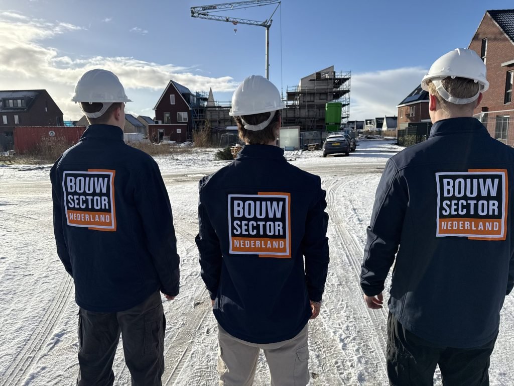 Drie vakmensen van Bouwsector Nederland met witte helm en logo op de rug kijken naar nieuwe woningen in de steigers
